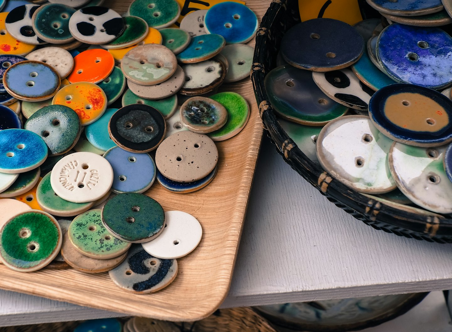 Handmade ceramic buttons displayed in a wooden tray and basket.