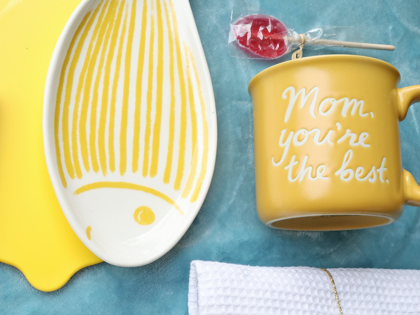 Yellow mug and fish plate with lollipop on blue fabric.